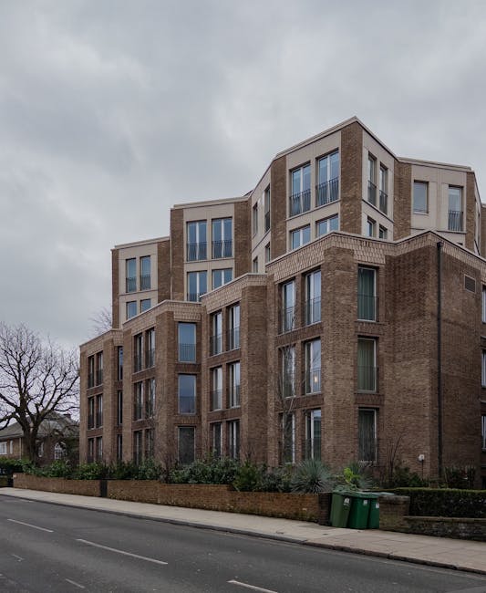A multi-storey residential building with a modern brick exterior and large windows facing the street, situated in Hampstead. In front of the building, a paved pavement runs alongside a low brick wall 